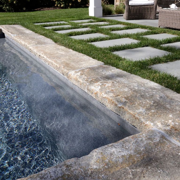 Application image for Reclaimed Granite Curbstone - Pool Coping. The image shows this product being used in a pool coping application. The surface finish shown is a combination of split-face with flat plane, weathered and worn. The dominant color shown is gray; with beige, brown, orange/rust, white, tan and cream secondaries. The color mix creates a warm feeling. Regular and speckled color patterns.