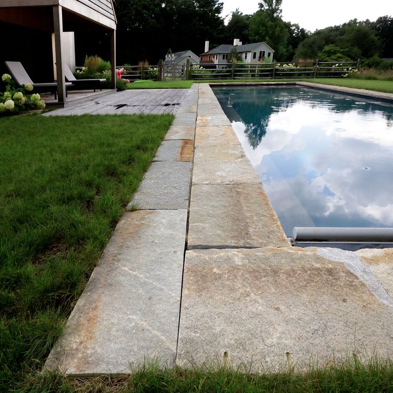 Application image for Granite - Reclaimed Curbstone - Pool Coping. The image shows this product being used for pool coping and pool deck pavers. The surface finish shown is . The dominant color shown is gray; with beige, brown, orange/rust and tan secondaries. The color mix creates a warm feeling. Speckled and blotched color patterns.
