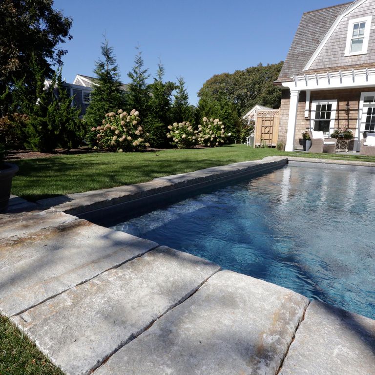 Application image for Reclaimed Granite Curbstone - Pool Coping. The image shows this product being used in a pool coping application. The surface finish shown is a combination of split-face with flat plane, weathered and worn. Dominant colors shown are black, blue and gray; with beige, brown, orange/rust and white secondaries. The color mix creates a warm feeling. Regular and speckled color patterns.