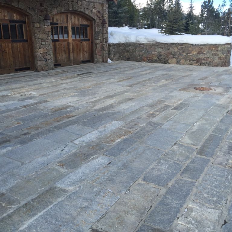Application image for Granite - Reclaimed Second Generation Curbstone - Plank Pavers. The image shows this product being used in a driveway pavers application. Dominant colors shown are blue and gray; with brown, green, purple and white secondaries. Exhibits 