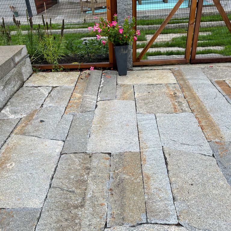 Application image for Reclaimed Second Generation Granite Curbstone Plank Pavers. The image shows this product being used for patio pavers and pool deck pavers. The surface finish shown is a combination of split-face with flat plane, weathered and worn. The dominant color shown is gray; with orange/rust and tan secondaries. Exhibits 