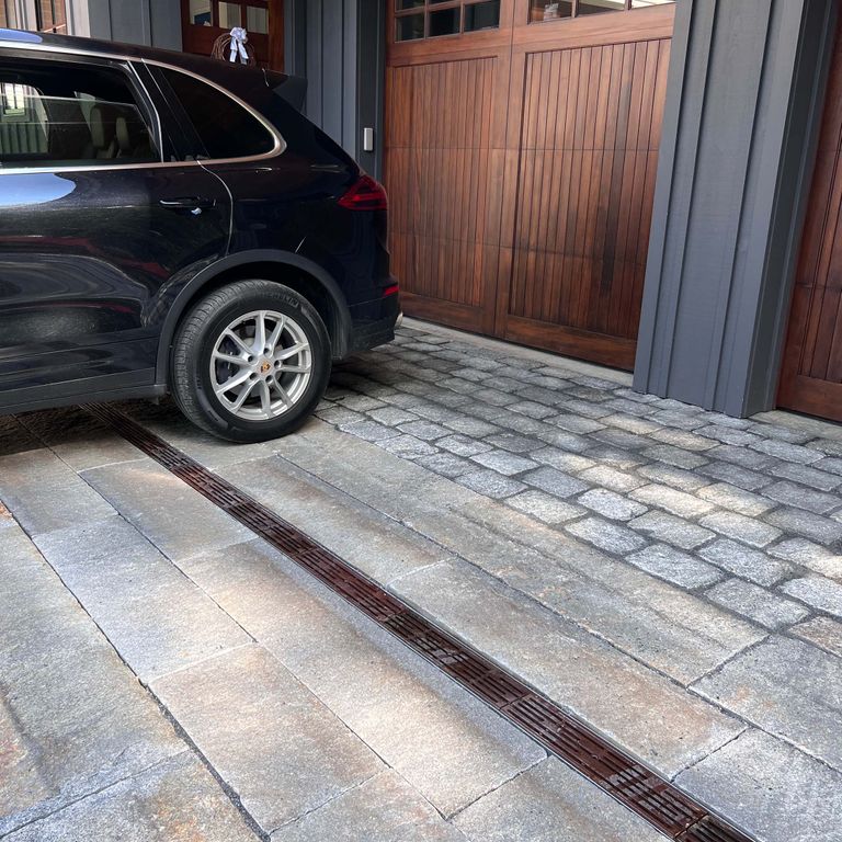 Application image for Reclaimed Third Generation Granite Curbstone Plank Pavers. The image shows this product being used in a driveway pavers application. The surface finish shown is a combination of split-face with flat plane and weathered. The dominant color shown is gray. The color mix creates a cool feeling. Regular and fine speckled color patterns.