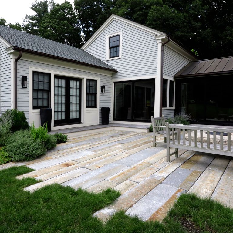 Application image for Reclaimed Third Generation Granite Curbstone Plank Pavers. The image shows this product being used in a patio pavers application. The surface finish shown is a combination of split-face with flat plane, weathered and worn. The dominant color shown is gray; with beige, blue, orange/rust, purple, white, tan and cream secondaries. The color mix creates a warm feeling. Regular, fine speckled and blotched color patterns.