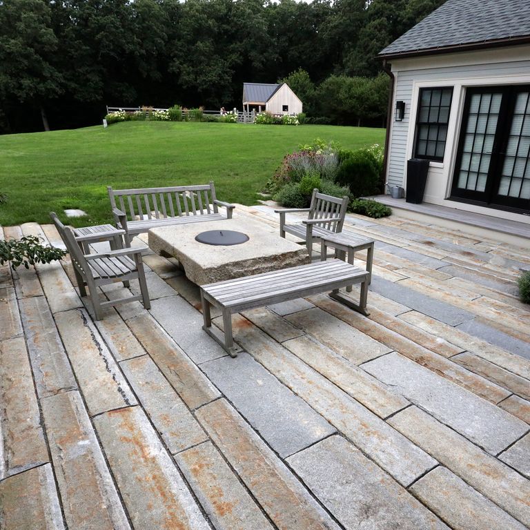 Application image for Reclaimed Third Generation Granite Curbstone Plank Pavers. The image shows this product being used in a patio pavers application. The surface finish shown is a combination of split-face with flat plane, weathered and worn. The dominant color shown is gray; with beige, blue, brown, orange/rust, purple, white, tan and cream secondaries. The color mix creates a warm feeling. Regular, fine speckled and blotched color patterns.