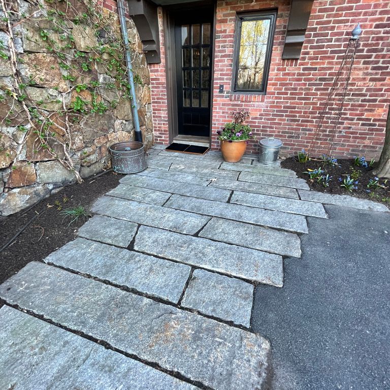 Application image for Reclaimed Third Generation Granite Curbstone Plank Pavers. The image shows this product being used in a path pavers application. The surface finish shown is a combination of weathered and worn. The dominant color shown is gray; with a brown secondary. The color mix creates a cool feeling. Speckled color pattern.