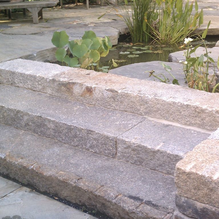 Application image for Reclaimed Second Generation Granite Curbstone Steps - Split Face Riser. The image shows this product being used in a monolithic steps application. This is a landscape stone for outdoor commercial and residential applications. Suitable for general use, freeze-thaw conditions, low heat absorption surfaces, high traffic areas and low slipperiness surfaces situations. Higher to high on the price spectrum.