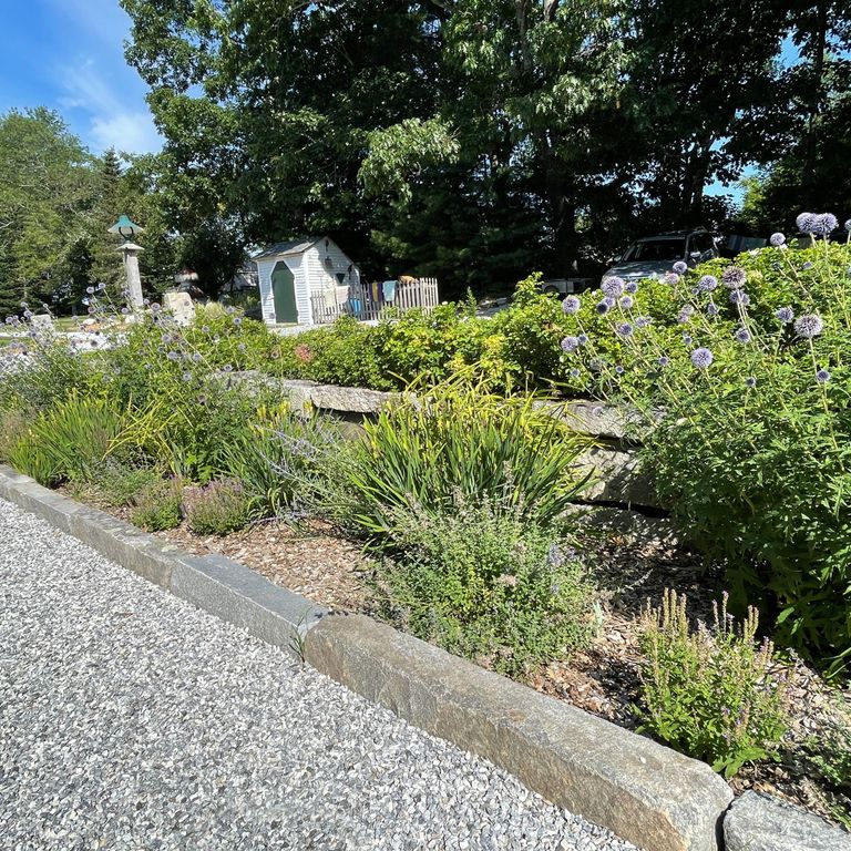Application image for Reclaimed First Generation Granite Curbstone - Edging. The image shows this product being used in a landscape curbing & edging application. The surface finish shown is a combination of weathered and worn. The dominant color shown is gray; with a tan secondary. The color mix creates a warm feeling.