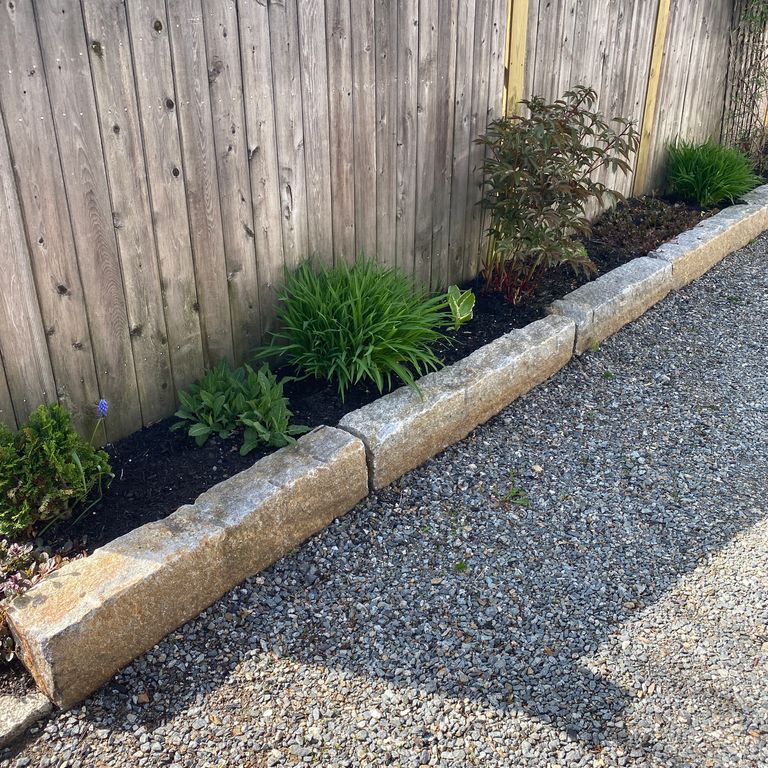 Feature image for Reclaimed Granite Curbstone - Junior Edging. The image shows this product being used in a landscape curbing & edging application. The dominant color shown is gray; with beige, brown, orange/rust, white, tan and cream secondaries. The color mix creates a warm feeling. Speckled and blotched color patterns.