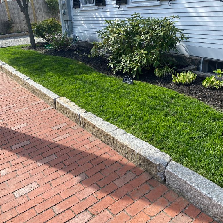 Application image for Reclaimed Granite Curbstone - Junior Edging. The image shows this product being used in a landscape curbing & edging application. This is a landscape stone for outdoor commercial and residential applications. Suitable for general use, freeze-thaw conditions, low heat absorption surfaces, high traffic areas, low slipperiness surfaces and high heel compatibilty situations. Moderate to higher on the price spectrum.