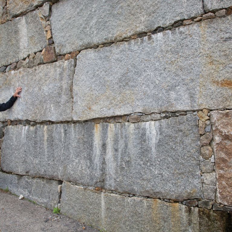 Feature image for Reclaimed Granite Bridge Blocks - Retaining Walls. The image shows this product being used in a landscape wallstone application. The design pattern shown is dimensional squares & rectangles. The dominant color shown is gray; with beige, brown, orange/rust, white and tan secondaries. Exhibits 