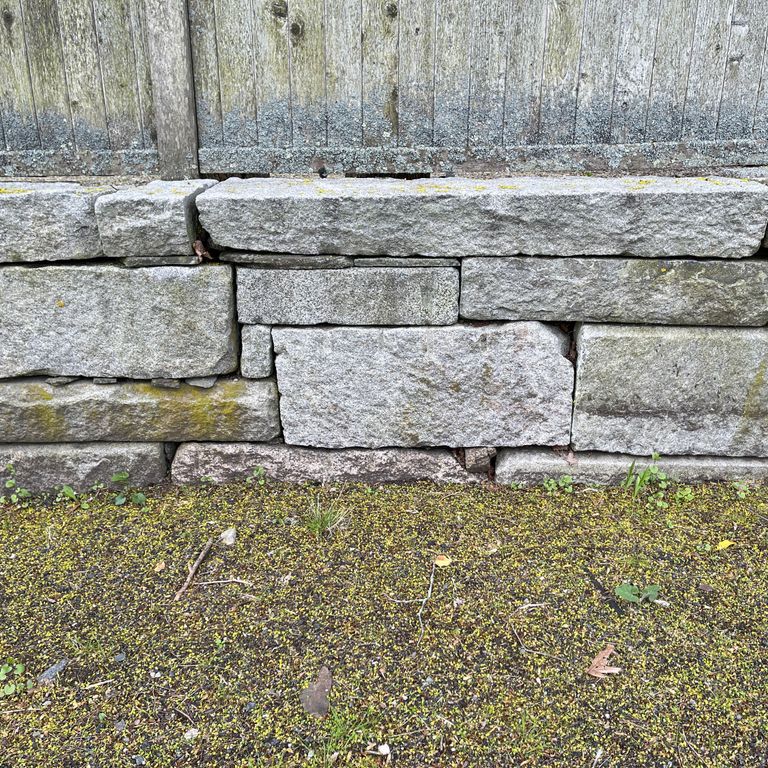 Application image for Reclaimed Granite Block Wallstone - Split Block Mix. The image shows this product being used in a landscape wallstone application. The surface finish shown is a combination of split-face and weathered. The dominant color shown is gray; with a brown secondary. The color mix creates a cool feeling. Speckled color pattern.