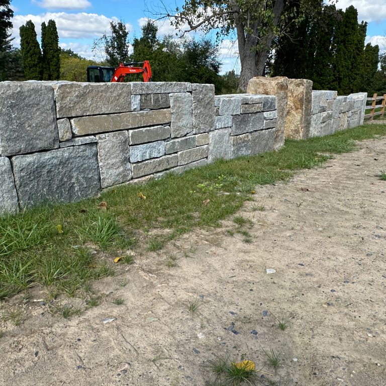 Application image for Granite - Reclaimed Block Wallstone - Block Mix. The image shows this product being used in a landscape wallstone application. The dominant color shown is gray.