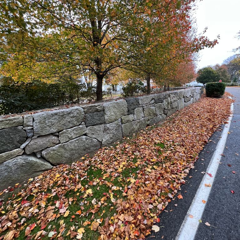 Feature image for Granite - Reclaimed New England Quarry Tailings - Oversized Wallstone. The image shows this product being used in a landscape wallstone application. The dominant color shown is gray. The color mix creates a cool feeling.