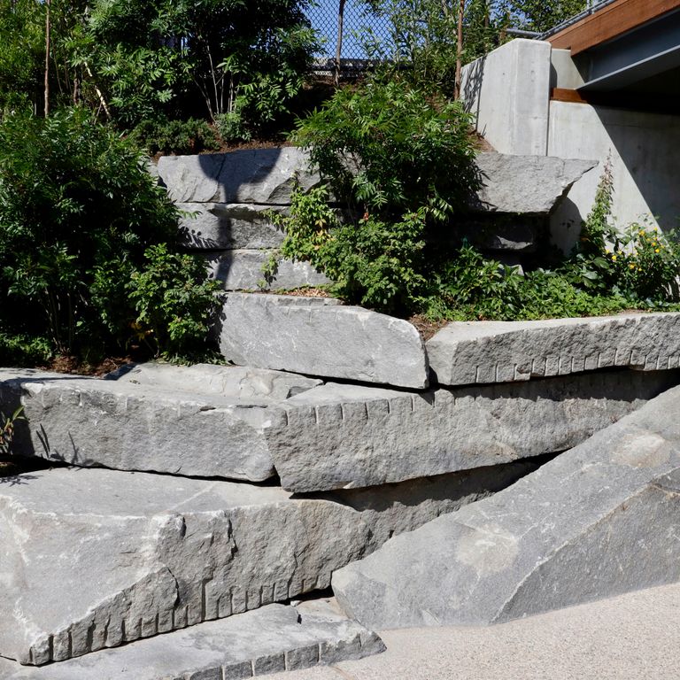 Application image for Reclaimed New England Granite Quarry Tailings - Oversized Wallstone. The image shows this product being used in a landscape wallstone application. Dominant colors shown are black and gray. The color mix creates a warm feeling.
