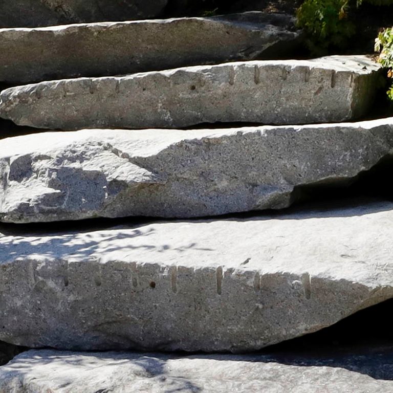 Close-up image for Reclaimed New England Granite Quarry Tailings - Steps and Landings. The surface finishes shown are split-face with rough plane and weathered. The dominant color shown is gray; with purple and white secondaries. The color mix creates a cool feeling. Regular, speckled and cloudy color patterns.