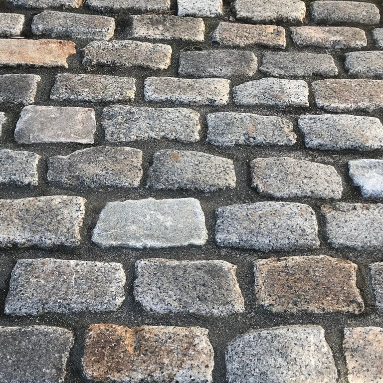 Best close-up image for Reclaimed New England Granite Cobblestones - Medium Pavers. The image shows this product being used in a driveway pavers application. The surface finish shown is a combination of weathered and worn. The dominant color shown is gray; with beige, brown, orange/rust, white and cream secondaries. The color mix creates a warm feeling. Swirled, speckled and blotched color patterns. Contains some mica and mineral inclusions.