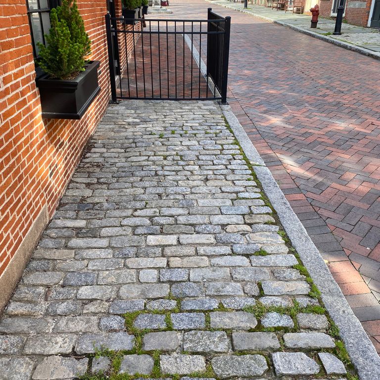 Application image for Reclaimed New England Granite Cobblestones - Medium Pavers. The image shows this product being used in a path pavers application. The surface finish shown is a combination of weathered and worn. The dominant color shown is gray; with a white secondary. The color mix creates a cool feeling. Speckled color pattern.