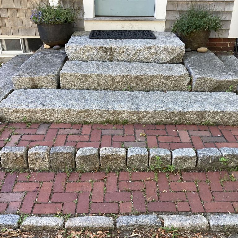 Application image for Reclaimed New England Granite Cobblestones - Medium Edging. The image shows this product being used in a landscape curbing & edging application. The surface finish shown is a combination of weathered and worn. The dominant color shown is gray; with brown, white and tan secondaries. The color mix creates a cool feeling. Regular, speckled and blotched color patterns.