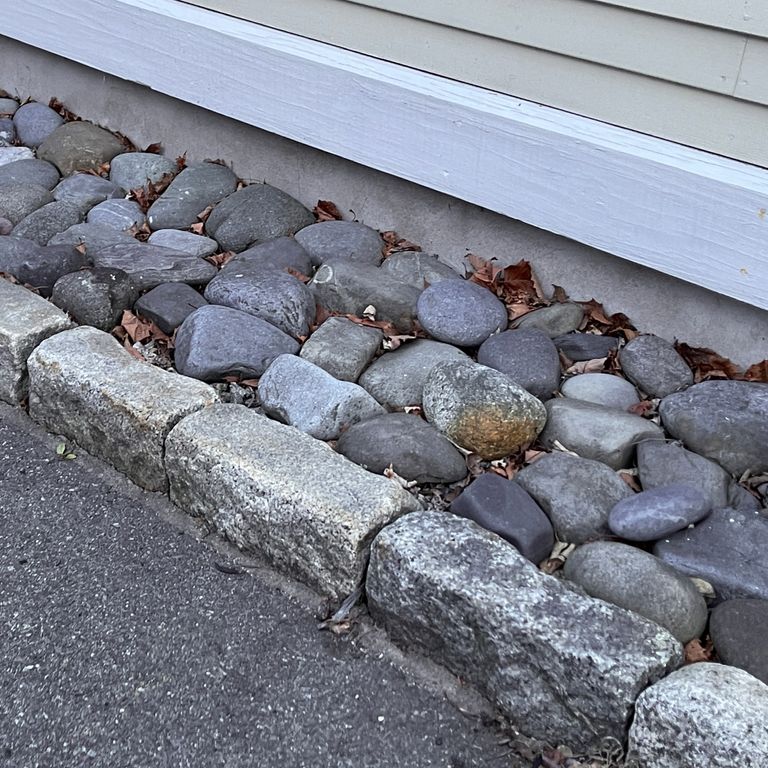 Best close-up image for Reclaimed New England Granite Cobblestones - Jumbo Edging. The image shows this product being used in a landscape curbing & edging application. The surface finish shown is a combination of weathered and worn. The dominant color shown is gray; with a brown secondary. The color mix creates a cool feeling. Regular, speckled and blotched color patterns.