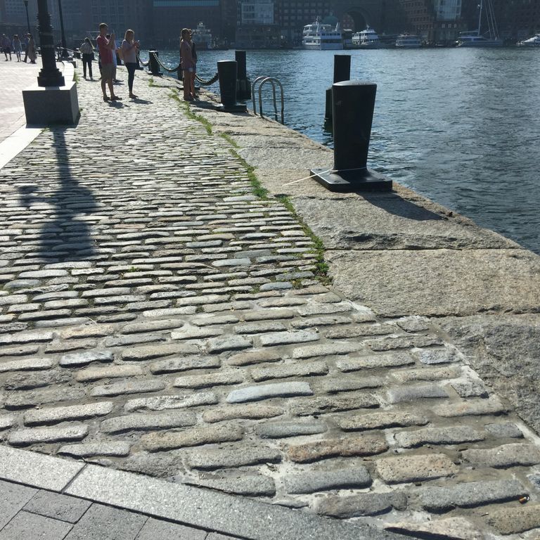 Feature image for Reclaimed New England Cobblestones - Jumbo Worn Top. The image shows this product being used in a public area application. The dominant color shown is gray; with beige, brown, green, white and cream secondaries. Regular and speckled color patterns.
