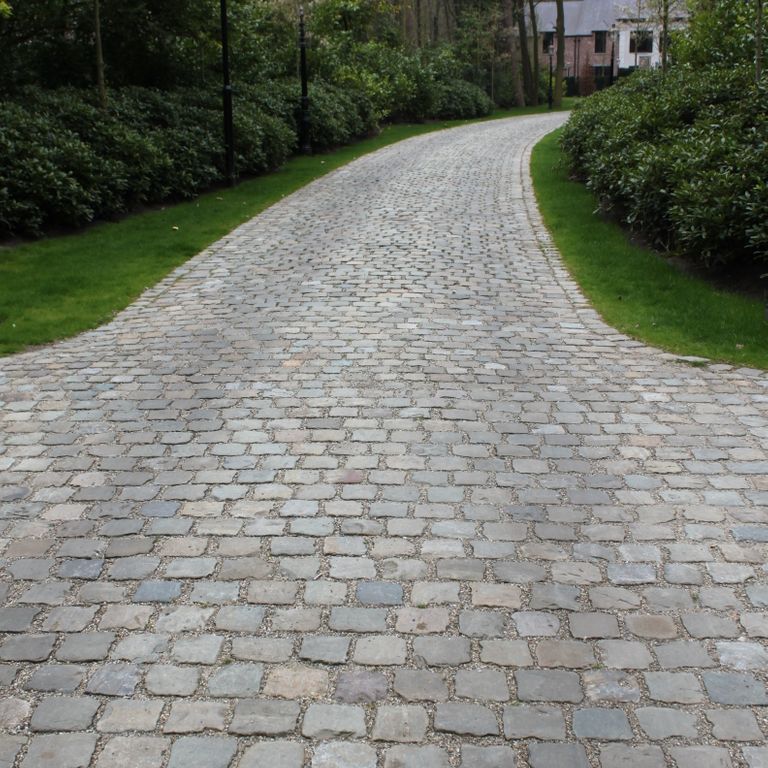 Application image for Reclaimed European Porphyry Cobblestones - Rectangle - Worn. The image shows this product being used in a driveway pavers application. The surface finish shown is . Dominant colors shown are black and gray. The color mix creates a cool feeling.
