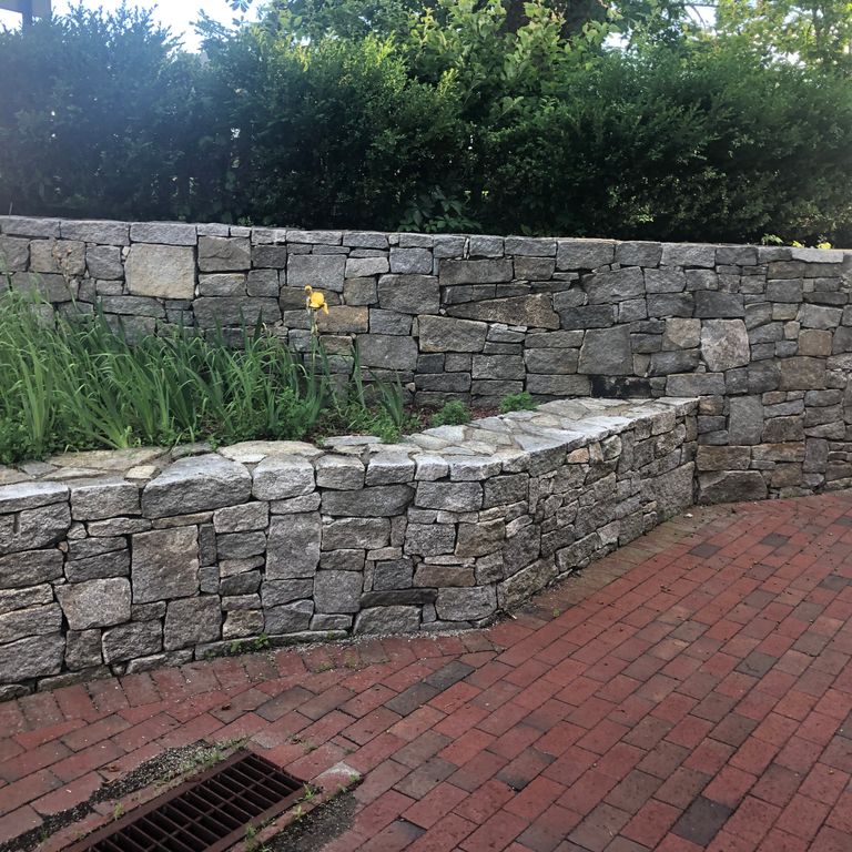 Application image for Granite - Reclaimed New England Quarry Tailings - Wallstone. The image shows this product being used in a landscape wallstone application. The dominant color shown is gray.