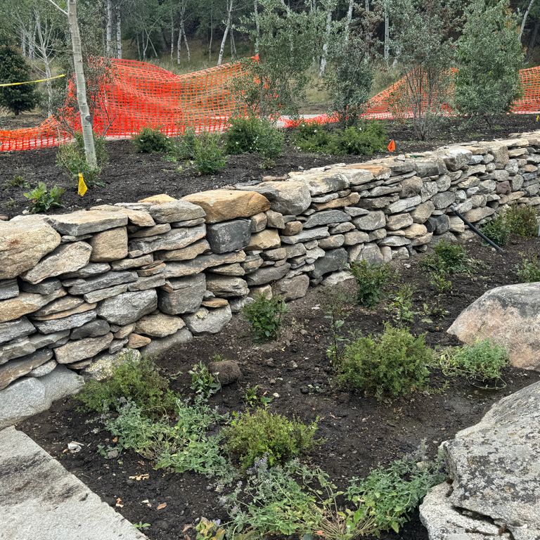 Application image for New England Fieldstone Flats - Wallstone. The image shows this product being used in a landscape wallstone application. The surface finish shown is weathered. The dominant color shown is gray.