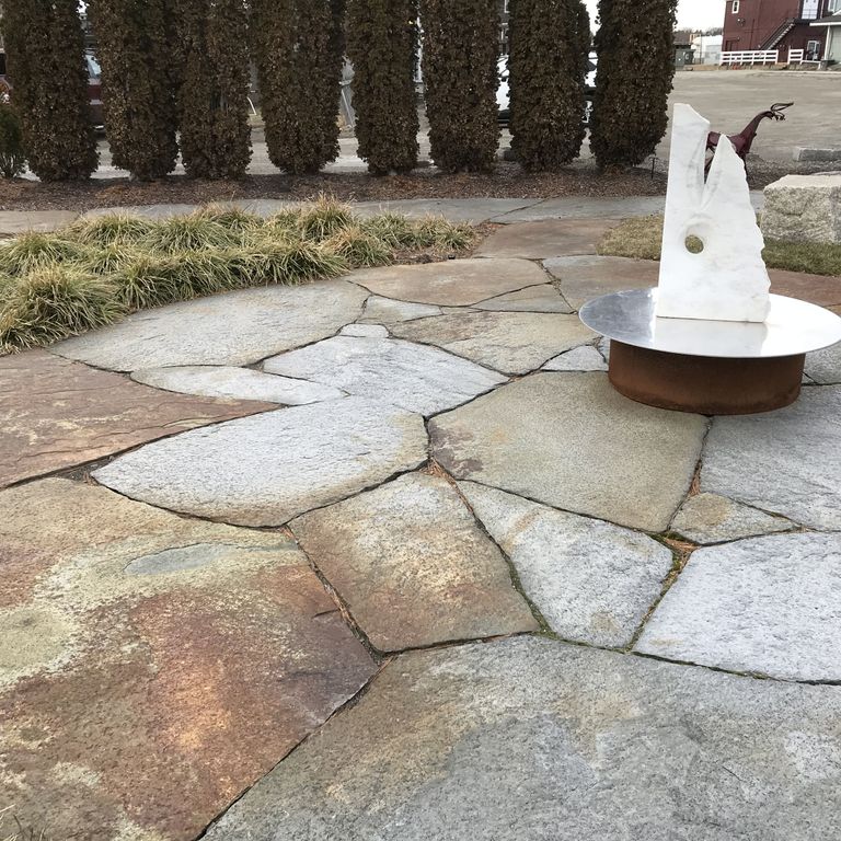 Application image for Goshen Stone - Irregular Flagstone. The image shows this product being used in a patio pavers application. The surface finish shown is split-face. Dominant colors shown are brown, green, gray and orange/rust. The color mix creates a warm feeling. Regular and blotched color patterns.