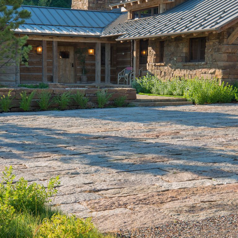 Application image for Reclaimed Granite Rustic Plank Pavers. The image shows this product being used in a driveway pavers application. The surface finish shown is a combination of split-face with flat plane and weathered. Dominant colors shown are beige, gray and tan; with brown, orange/rust, purple and cream secondaries. The color mix creates a warm feeling.