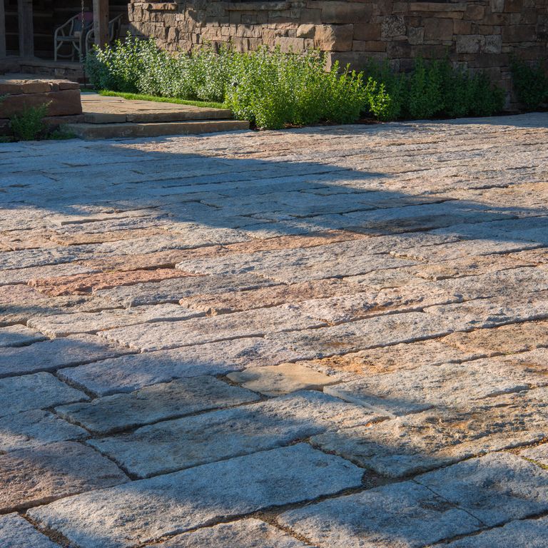 Application image for Reclaimed Granite Rustic Plank Pavers. The image shows this product being used in a driveway pavers application. The surface finish shown is a combination of split-face with flat plane and weathered. The dominant color shown is beige; with brown, gray, orange/rust, purple and cream secondaries. The color mix creates a warm feeling. Regular color pattern.