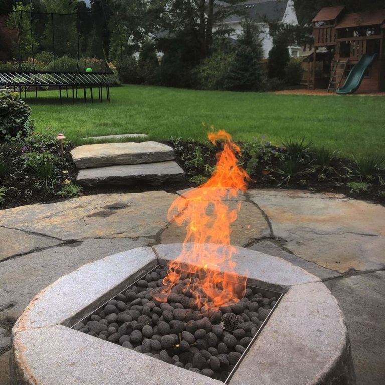 Feature image for Reclaimed D-Radius Curbstone Fire Pit. The image shows this product being used in an outdoor fire concepts application. The surface finish shown is a combination of weathered and worn. Dominant colors shown are brown and gray; with an orange/rust secondary. The color mix creates a cool feeling. Regular and blotched color patterns.
