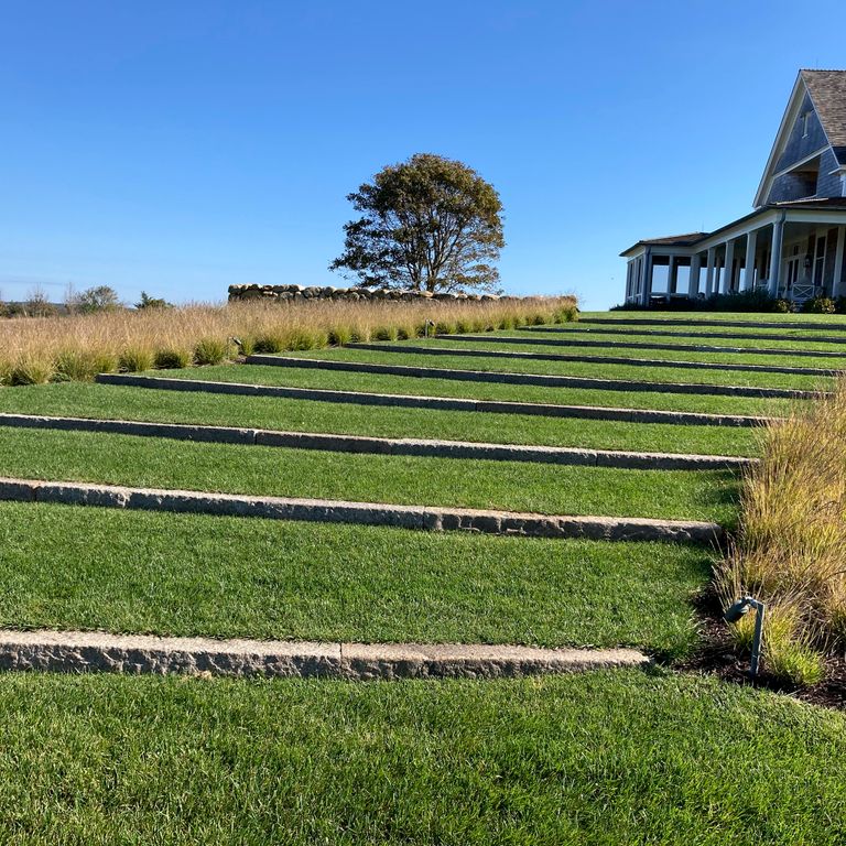 Application image for Reclaimed First Generation Granite Curbstone - Lawn Steps. The image shows this product being used in a monolithic steps application. The surface finish shown is a combination of weathered and worn. Dominant colors shown are gray and tan; with an orange/rust secondary. The color mix creates a cool feeling.