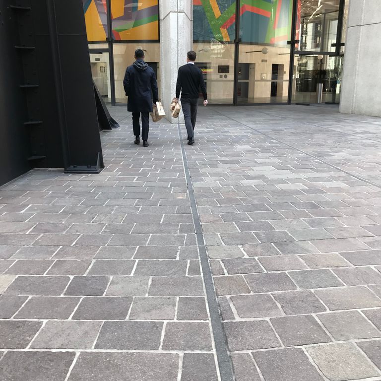 Feature image for Porphyry - Natural Surface - Mixed Gray - Pavers. The image shows this product being used in a public area application. The dominant color shown is gray; with beige, blue, brown, green, orange/rust, purple, white, tan and cream secondaries. Speckled color pattern.