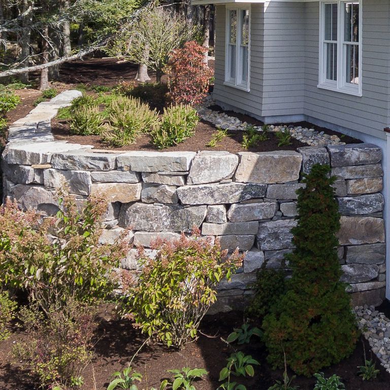 Feature image for Black Mountain Granite Natural - Wallstone. The image shows this product being used in a landscape wallstone application. Design patterns shown are quarried-snapped random ashlar and quarried-snapped roughly square roughly rectangular with sharp edges. The dominant color shown is gray; with beige, blue, brown, orange/rust, purple, white and tan secondaries. Exhibits 