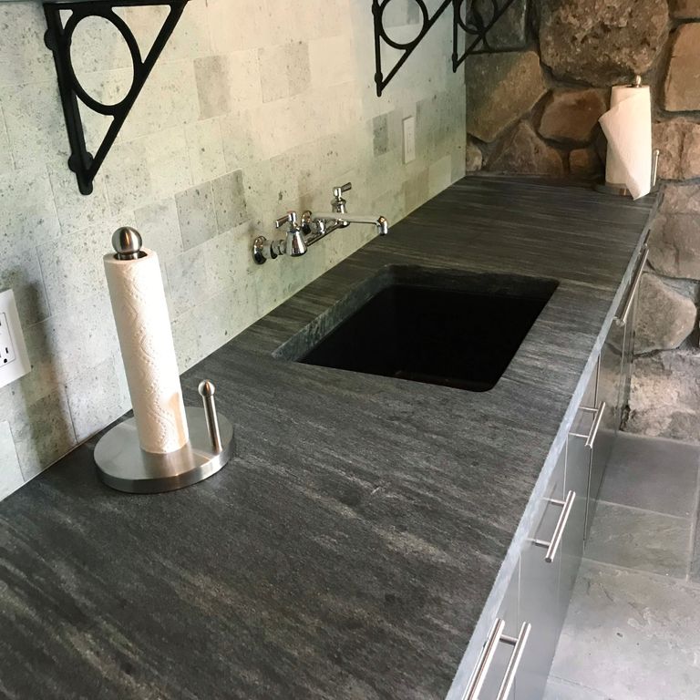 Feature image for Mystic Mountain Countertops. The image shows this product being used in a countertop slabs application. The dominant color shown is gray; with black, brown, green and tan secondaries. Exhibits 