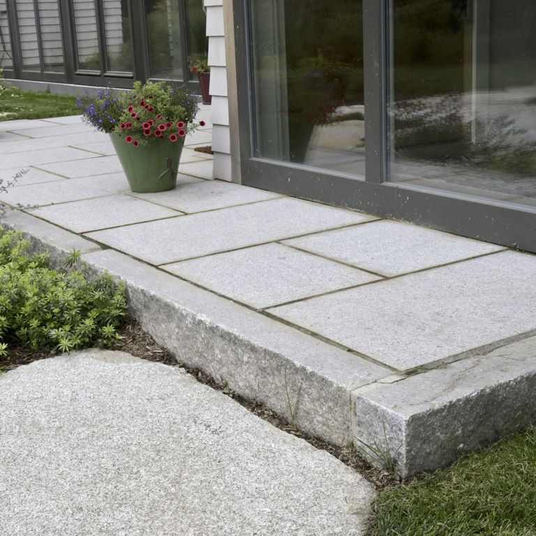 Application image for Granite - Reclaimed - Edging. The image shows this product being used in a landscape curbing & edging application. The surface finish shown is a combination of sawn, split-face with flat plane and weathered. The dominant color shown is gray; with beige, blue, purple and white secondaries. The color mix creates a cool feeling. Speckled color pattern.