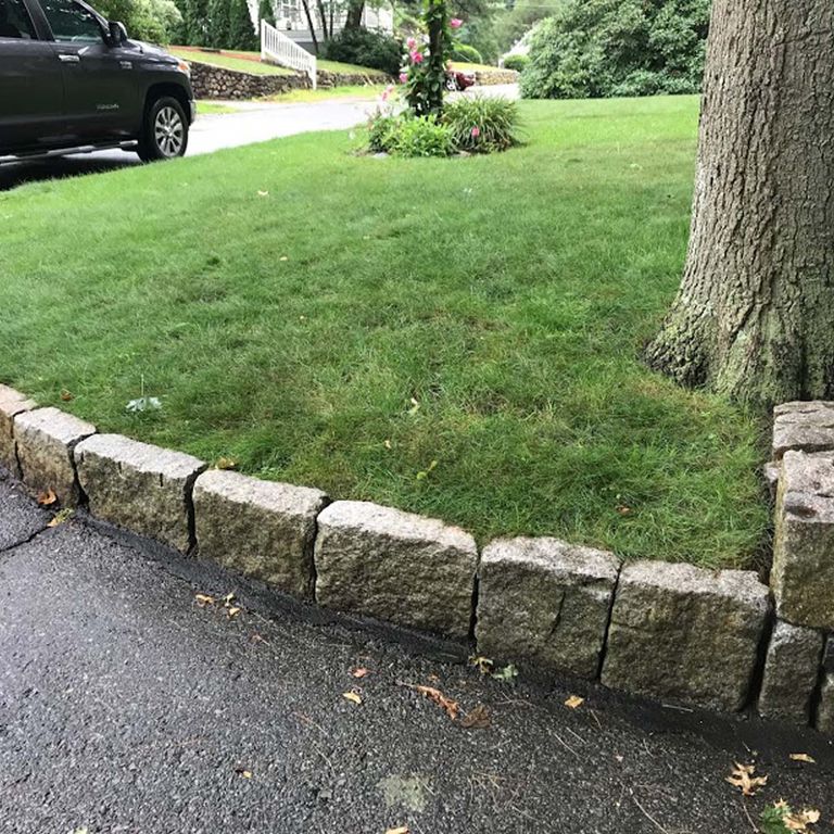 Feature image for Reclaimed New England Granite Cobblestones - Super Jumbo Edging. The image shows this product being used in a landscape curbing & edging application. The dominant color shown is gray; with beige, black, brown, orange/rust, purple, white and tan secondaries. Exhibits 