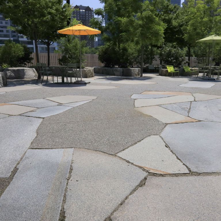 Feature image for Granite - New England Mix - Live Edge Paver. The image shows this product being used for patio pavers and public area. The surface finish shown is flamed. Dominant colors shown are beige and gray; with pink, purple, white and cream secondaries. Speckled color pattern.