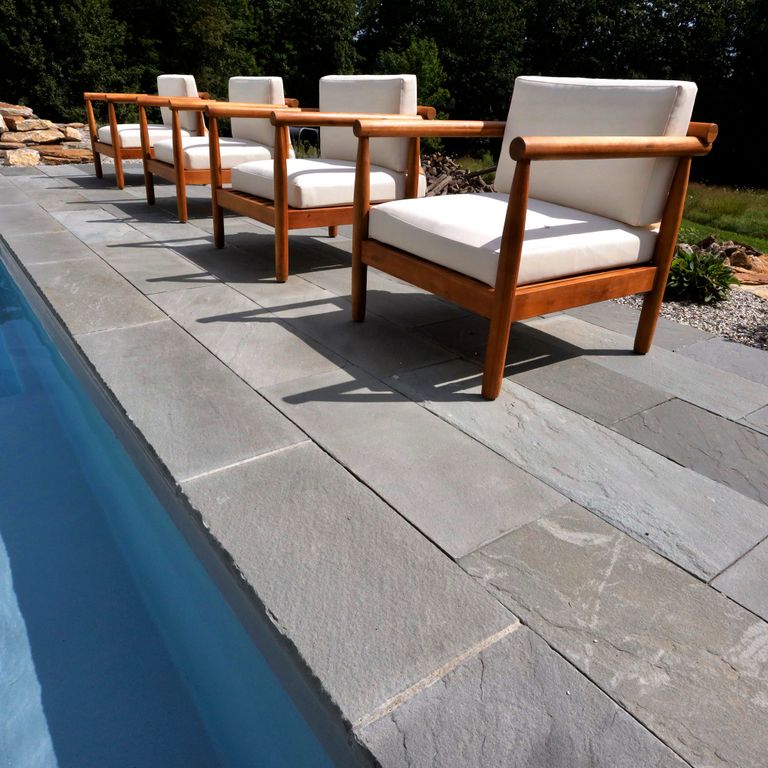 Application image for Bluestone Natural Cleft Blue/Gray - Dimensional Cut Pavers. The image shows this product being used for pool coping, patio pavers and pool deck pavers. The surface finish shown is natural cleft. Dominant colors shown are blue and gray; with beige, purple and white secondaries. The color mix creates a cool feeling. Regular color pattern.