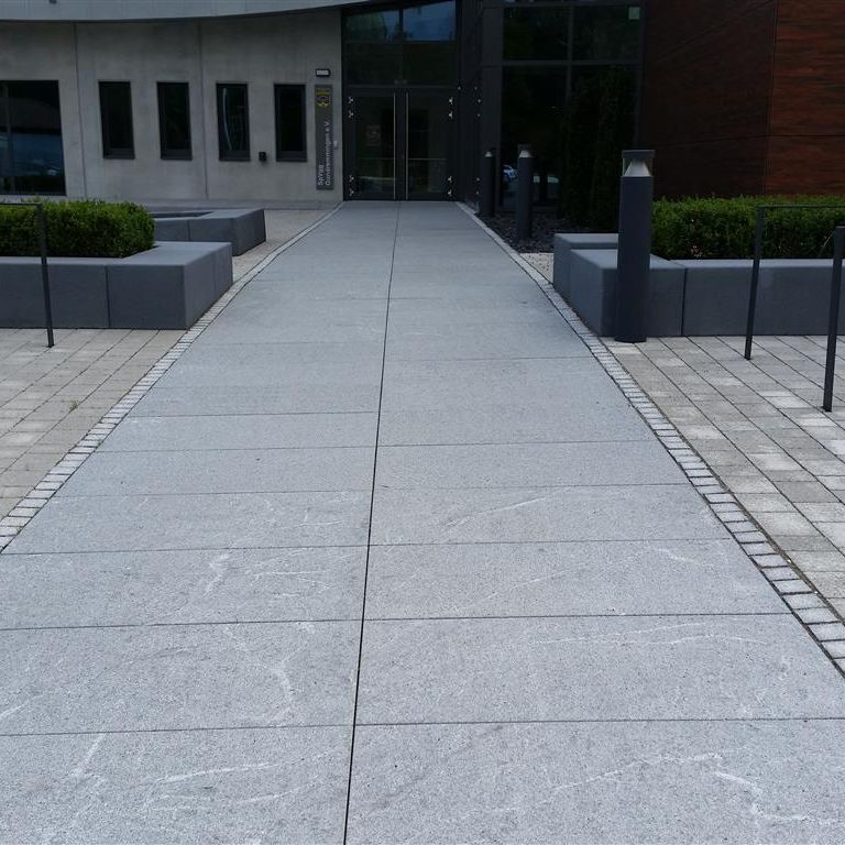Feature image for Granite - Republic Black - Pavers. The image shows this product being used in a path pavers application. Dominant colors shown are blue and gray; with a white secondary. Exhibits 