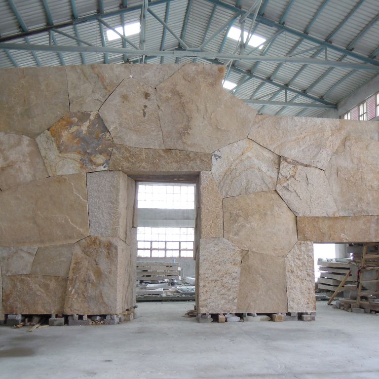 Feature image for Quarried Chinese Granite - Quarry Skin Veneer. The image shows this product being used for full bed veneer and interior cladding. The surface finish shown is split-face with flat plane. Dominant colors shown are beige, brown, gray and tan; with an orange/rust secondary. Exhibits 