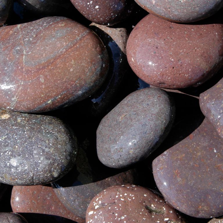 Best close-up image for Granite - Beach Pebbles - Natural Red. The surface finish shown is worn. Dominant colors shown are brown, gray and purple; with an orange/rust secondary. Streaked, speckled and blotched color patterns.