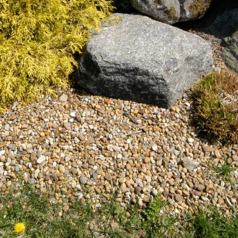 Feature image for Granite Beach Pebbles - Natural Tan. The image shows this product being used in a garden accents application. Dominant colors shown are brown and tan; with beige, gray, orange/rust, white and cream secondaries. The color mix creates a warm feeling. Speckled and fine speckled color patterns.