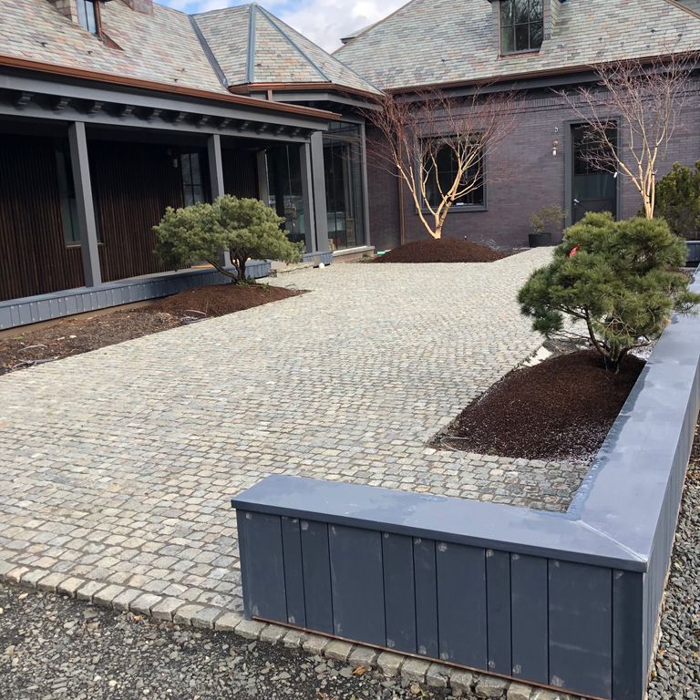 Application image for Reclaimed European Porphyry Cobblestones - Worn Cubes. The image shows this product being used in a patio pavers application. The surface finish shown is . The dominant color shown is gray. The color mix creates a warm feeling.