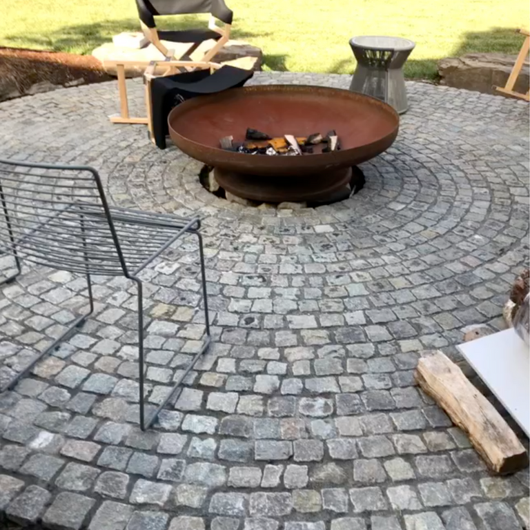 Application image for Reclaimed European Porphyry Cobblestones - Worn Cubes. The image shows this product being used in a patio pavers application. The surface finish shown is . The dominant color shown is gray. The color mix creates a warm feeling.