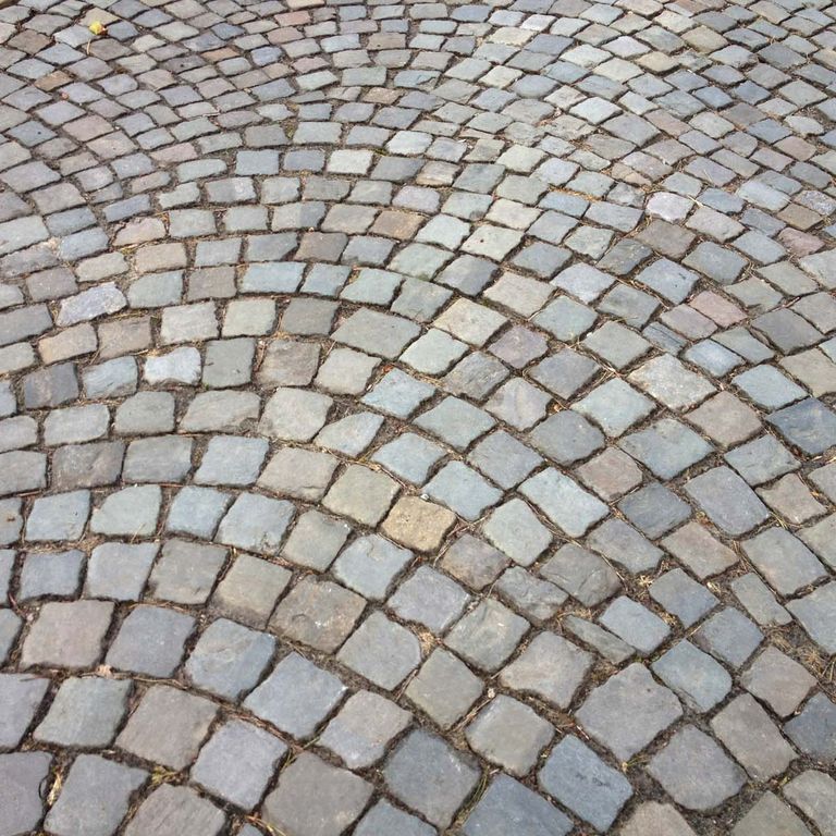 Application image for Reclaimed European Sandstone Cobblestones - Worn Cubes. The image shows this product being used in a driveway pavers application. The surface finish shown is . The dominant color shown is gray. The color mix creates a warm feeling.