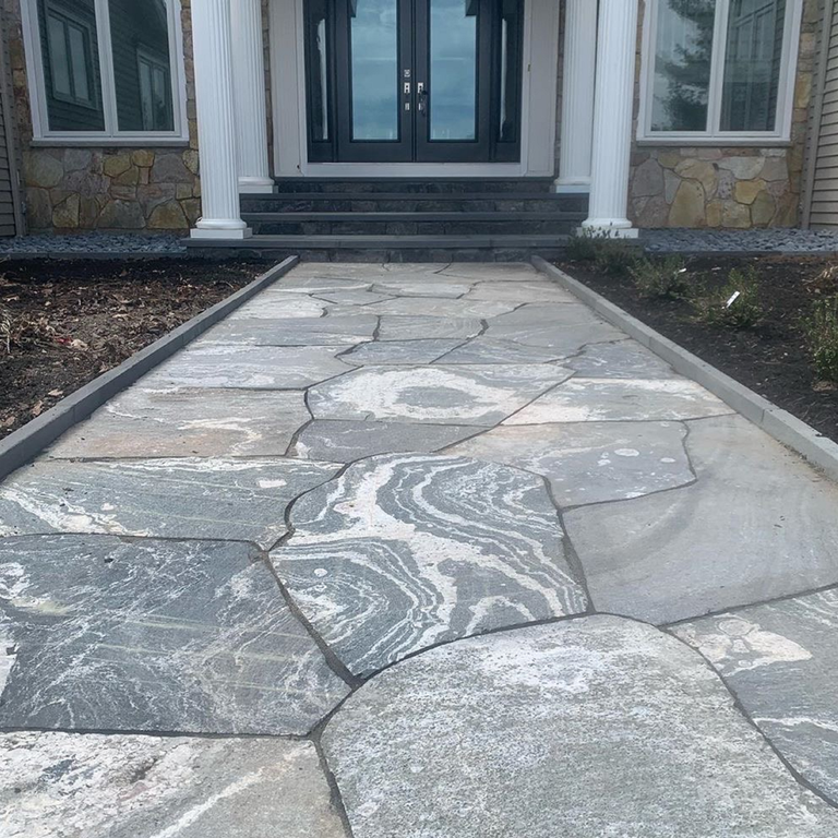 Feature image for American Mist Granite - Pavers. The image shows this product being used in a path pavers application. Dominant colors shown are blue and gray; with green and white secondaries. Exhibits 