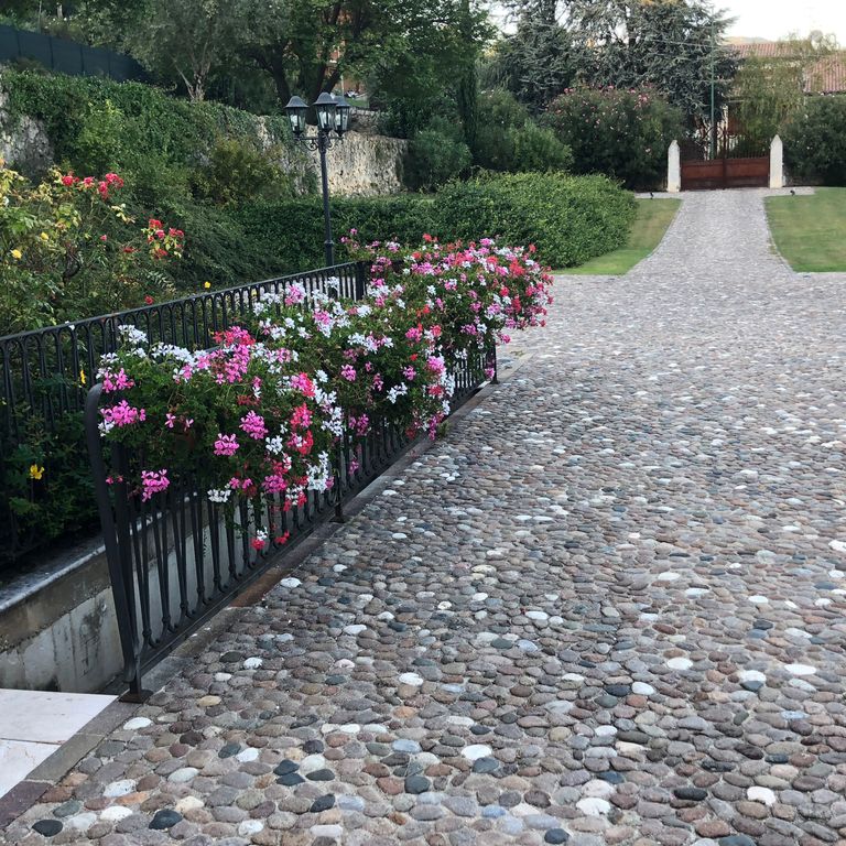 Feature image for River Rounds - Pavers. The image shows this product being used in a driveway pavers application. The dominant color shown is gray; with black, blue, brown, orange/rust, purple, white and tan secondaries. Fine speckled color pattern.