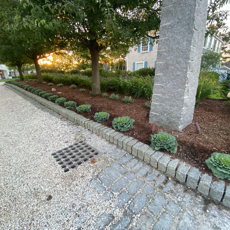 Application image for Gray Granite Cobblestone - Rectangles. The image shows this product being used in a landscape curbing & edging application. The surface finish shown is tumbled. The dominant color shown is gray; with a blue secondary. The color mix creates a cool feeling. Speckled color pattern. Contains some mica and mineral inclusions.