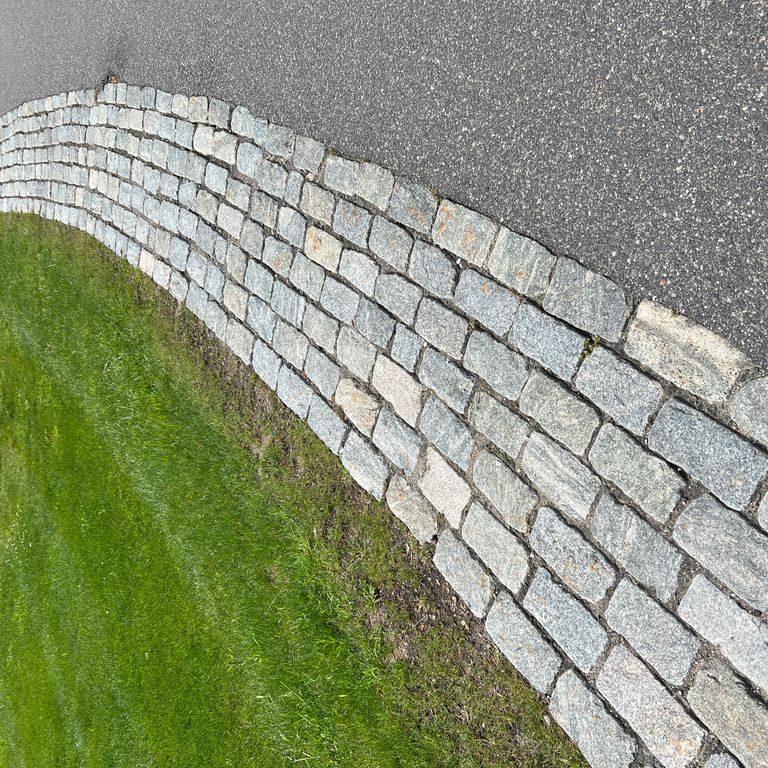 Application image for Granite - Cobblestones - Gray. The image shows this product being used in a driveway pavers application. The dominant color shown is gray. The color mix creates a cool feeling.